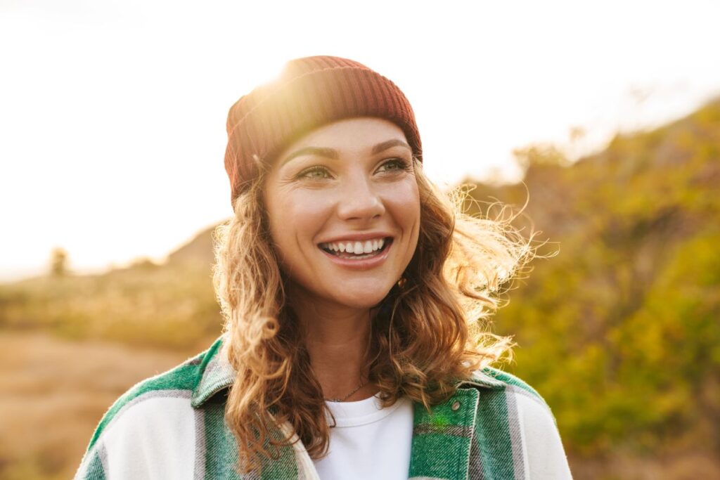 Junge Frau laechelt in herbstlicher Natur, als Symbolbild fuer Entspannung auf einer Parkbank
