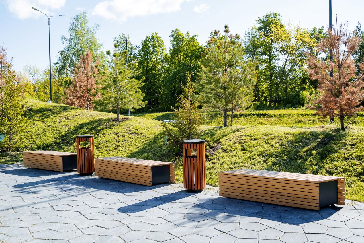 Mehrere moderne Parkbaenke aus Holz und Metall in urbaner Gruenanlage bei Sonnenschein