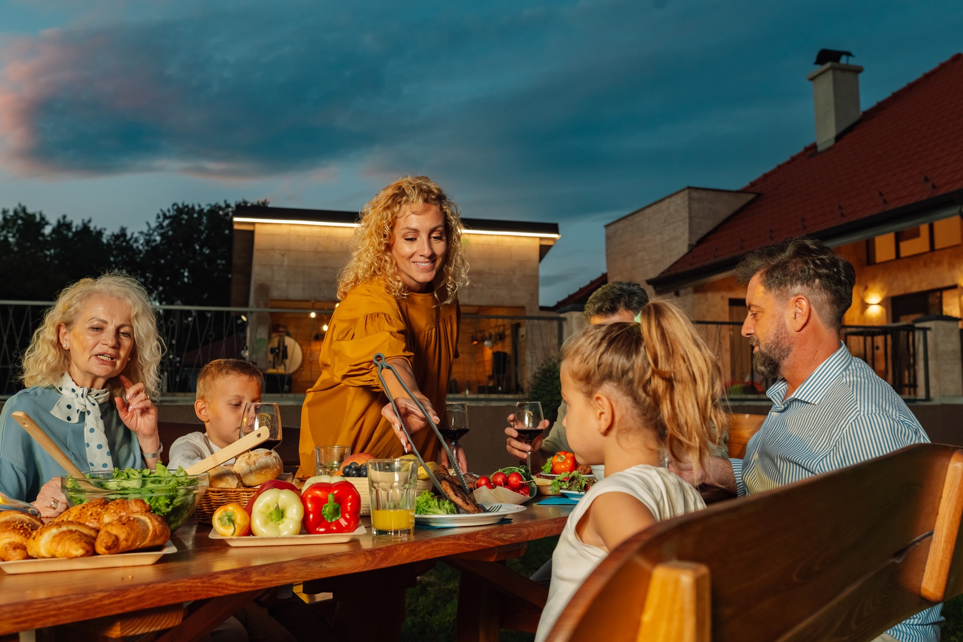 Mann grillt Fleisch, während Freunde an einer Bierbankgarnitur im Garten sitzen